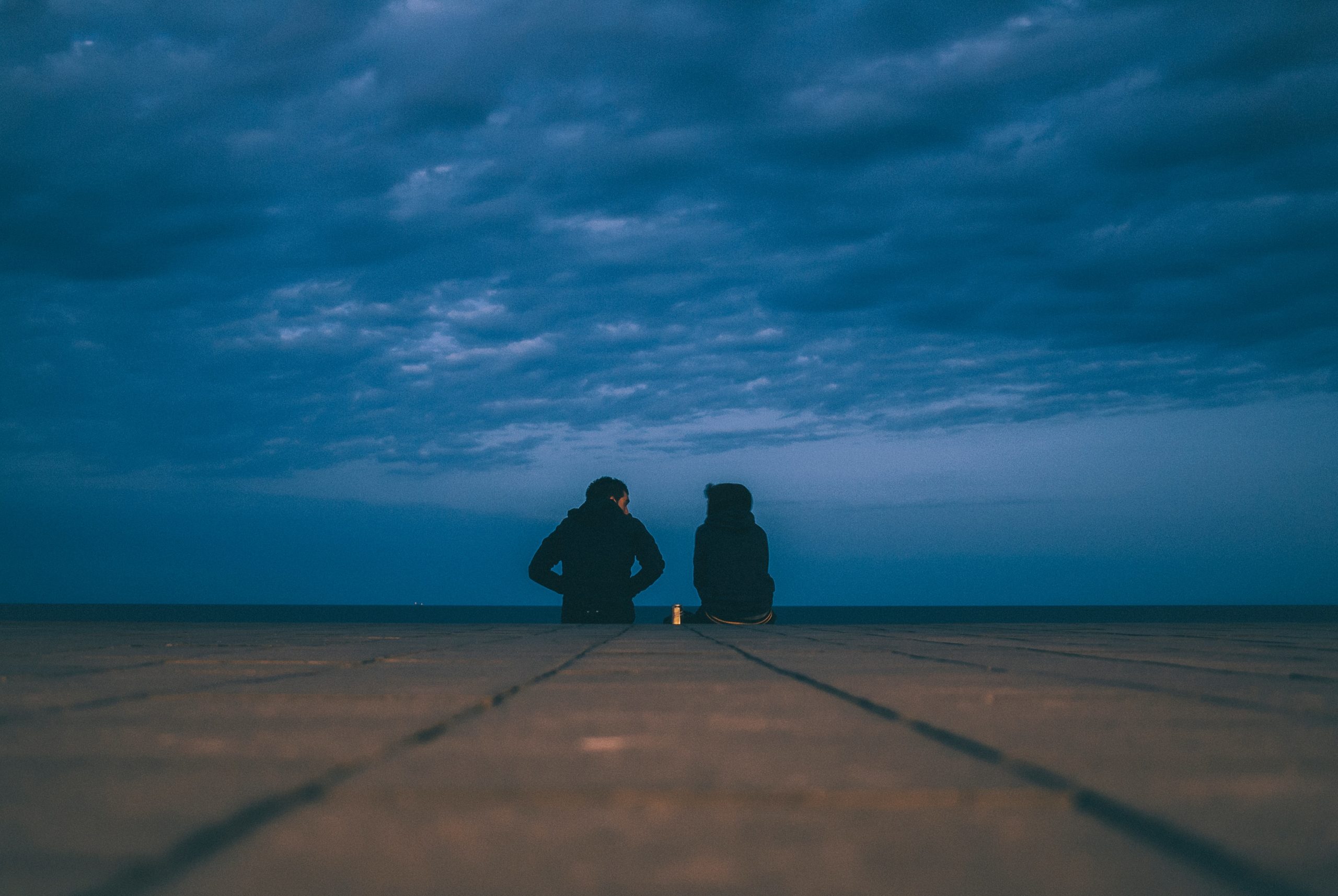 Two people sitting down facing away from the camera with hands in their pockets